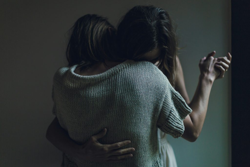 Dos mujeres se abrazan y se dan la mano, apoyando la cabeza en el hombro